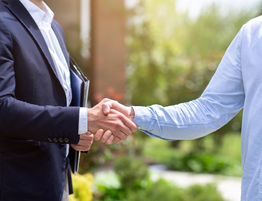 Men have a model house on hand,other hand is using a pen signing contract,background is a blurred condominium image.